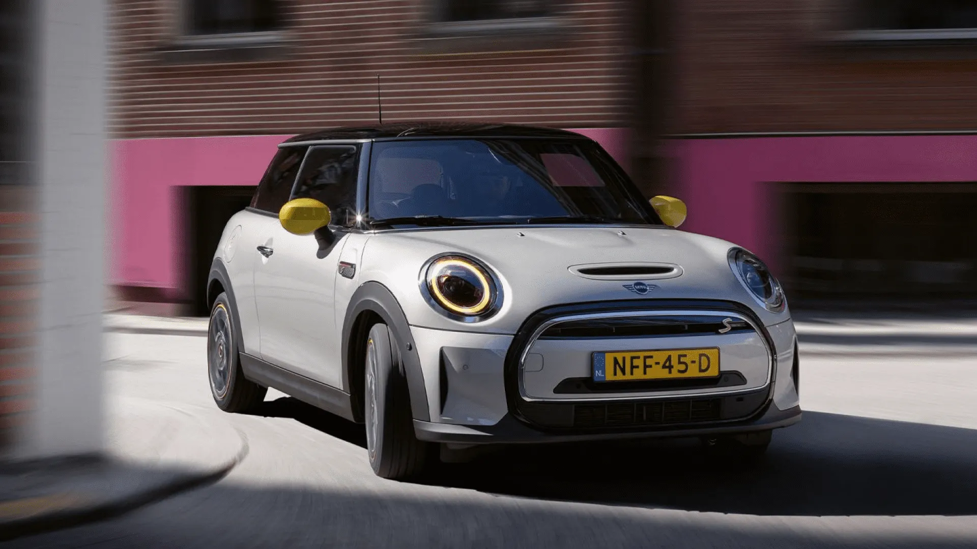 Mini claro con retrovisores amarillos maniobrando, uno de los coches pequeños para ciudad.