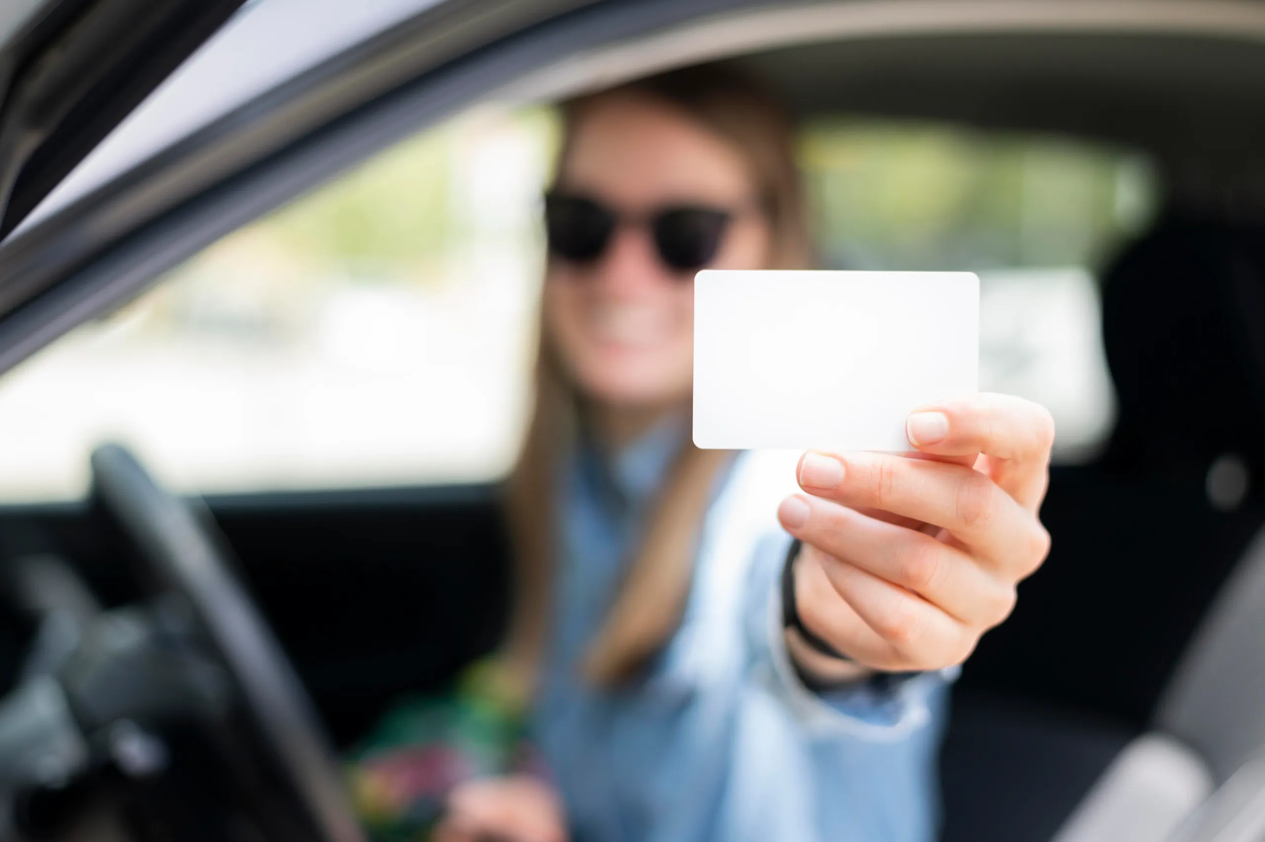 Joven sonriente mostrando su carnet de coche automático recién obtenido.