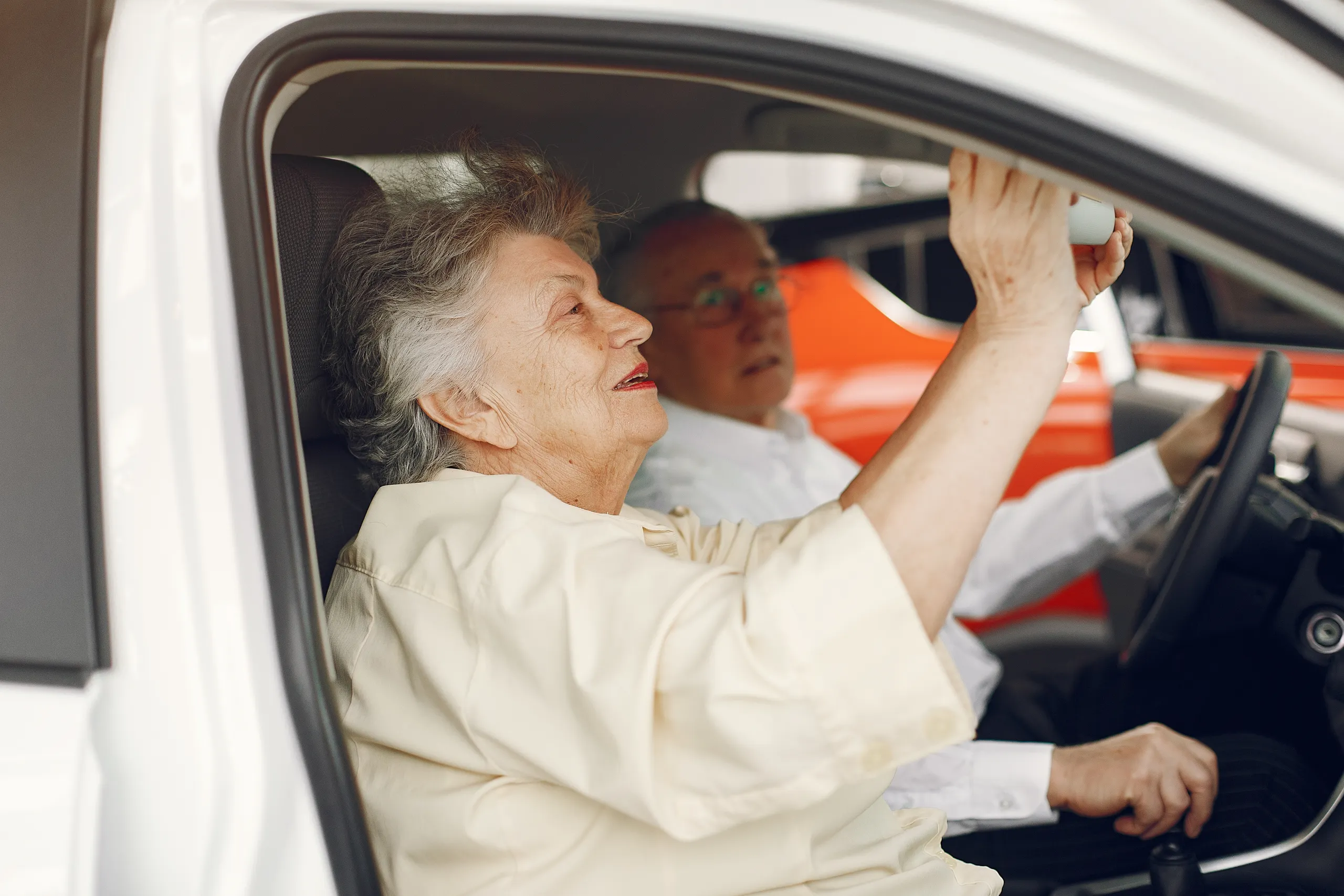 Mujer mayor ajusta el retrovisor de un coche Pareja mayor probando un coche ideal para personas mayores de 70 años en concesionario.