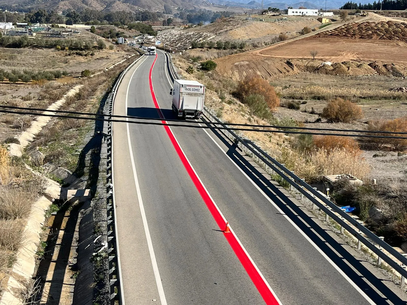 Línea roja en carretera con un camión en vía rural y un paisaje montañoso despejado.